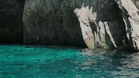 Calm turquoise water with small waves against rocky cliff Stock Footage 156227940