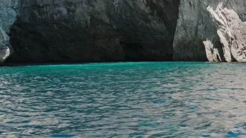 Calm turquoise water with small waves against rocky cliff Stock Footage 168415231