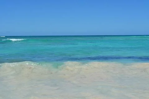 Calm Turquoise Waves Gently Touch the Sandy Shore Under a Bright Blue Sky Stock Photos