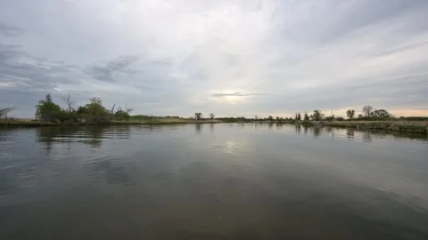 Calm water reflects gray clouds and grassy shore on a moody looking day Stock Footage 300895114