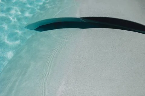 Calm water ripples over smooth sand beside a serene pool in bright sunlight Stock Photos