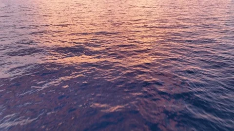Calm water surface reflects pink and orange hues during sunset over the ocean Stock Footage 338166255