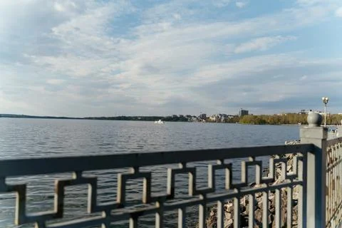 A calm waterfront scene featuring a lakeside railing in the foreground, with Stock Photos