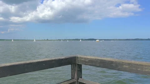 Calm waters and a cloudy sky viewed from a wooden pier extending over the l.. Vídeo Stock 281276692