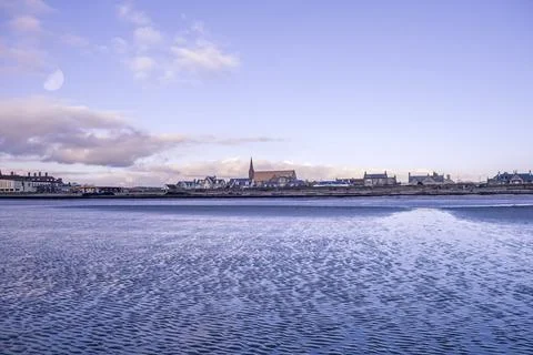 Calm waters reflect the distant town skyline Stock Photos