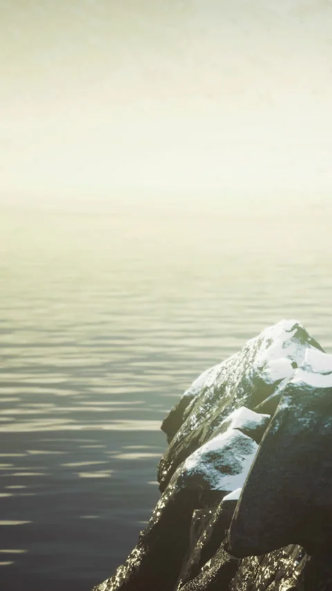 Calm waters reflect soft light over snowy rocks at dawn Stock Footage 334251574