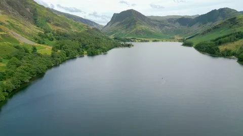 Calm waters reflect surrounding green hills and distant peaks Stock Footage 345523896