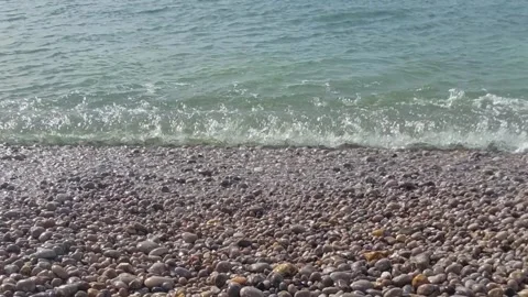 Calm waves wash over smooth stones at a serene beach in the early morning lig Stock Footage 310713580