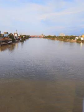 Calm wide river flowing through city landscape under clear bright blue sky Stock Photos
