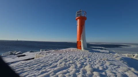 Calm winter scene features bright orange lighthouse overlooking icy coast with Stock Footage 328377715