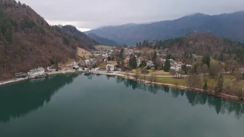 Calm winter waters at Lake Bled reflect mountains, forests, and cottages Stock Footage 336467676