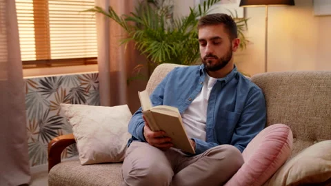 Calm Young Man Sitting n Bright Living Room At Home And Reading A Book Stock Footage 147003492
