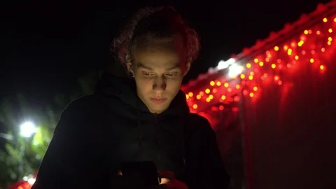 Calm young man using phone at Christmas night, fair red lights bg, 4k footage Stock Footage 98878691
