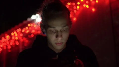 Calm young man using phone at New Year night, fair red lights bg, 4k footage Stock Footage 98878834