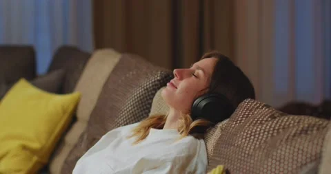 Calm young woman put on modern wireless headphones to relax on comfortable sofa Stock Footage 168259687