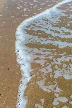 A calming close-up view of a sandy beach with foamy waves gently receding. Th Stock Photos