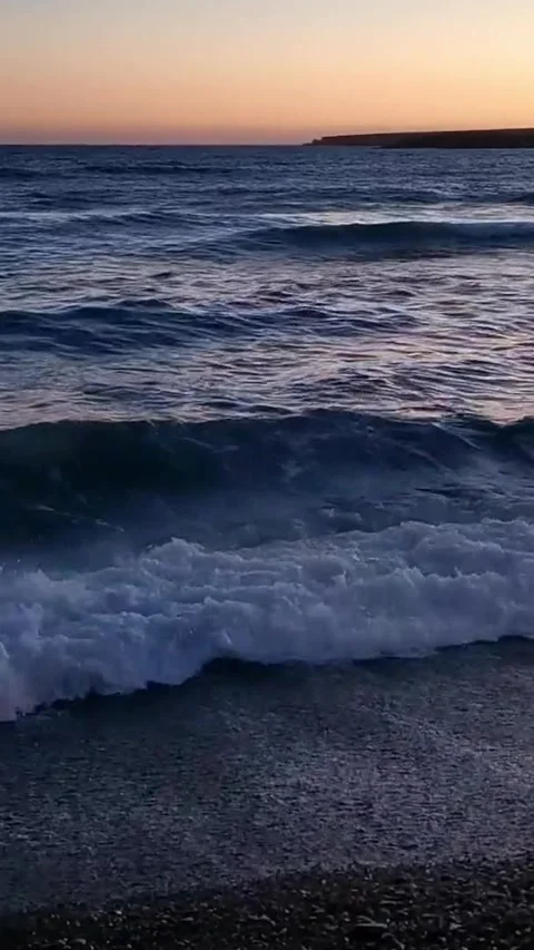 Calming ocean waves washing ashore on a dark pebble beach with a beautiful Stock Footage 344786341