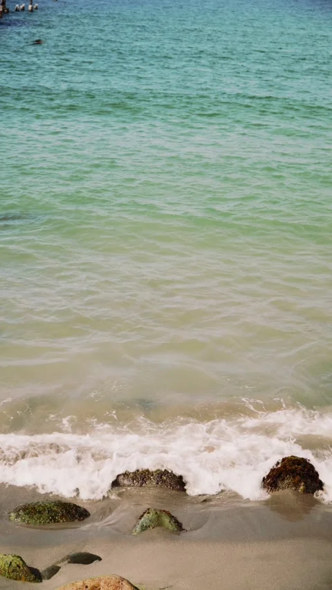 Calming ocean waves washing over a sandy beach with rocks Stock Footage 326225547