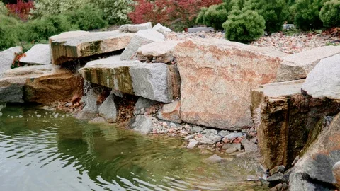 Calming Water Flow of Neat Artificial Waterfall with Pond and Plants and Flowers Stock Footage 112880061