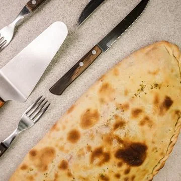 Calzone pizza on table and different cutlery Stock Photos