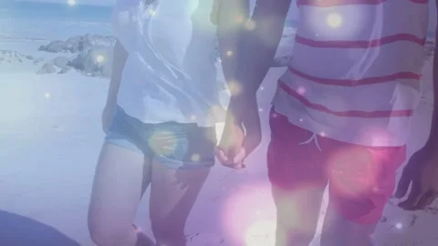 Cam tracking, couple walking hand-in-hand beachside, pink bokeh floating over Vídeo Stock 333936759