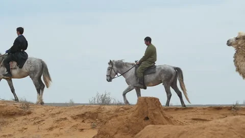 A camel caravan with a driver on a white camel and two riders on horseback. Stock Footage 218458955