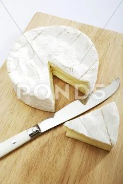 Camembert With A Piece Cut Out On A Wooden Board With Knife