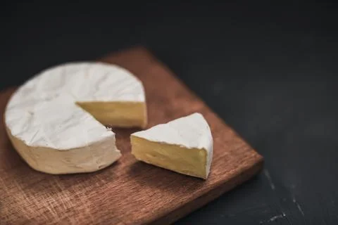 Camembert round cheese and a slice lie on a wooden board. grey background Stock Photos