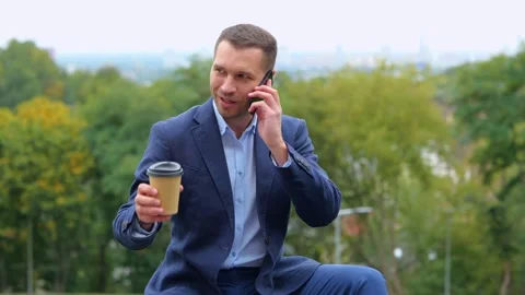 Camera approaching young businessman sitting outdoor chatting on smartphone and Stock Footage 254950360