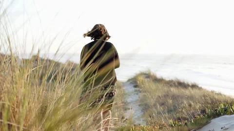 Camera behind foliage while Woman walks very slowly in the sand path. Stock Footage 116438164