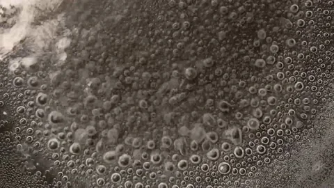 The camera captures a close-up of boiling water. The surface of the water Stock Footage 150242714