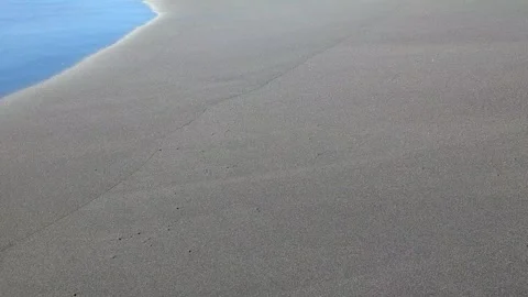 The camera captures a steady view of dark volcanic sand. Gentle ocean water.. Video stock 331179449