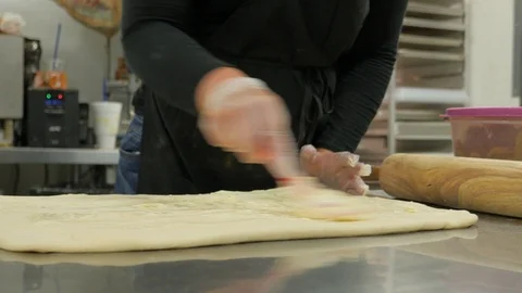 Camera circles around metal table with dough as woman spreads butter Stock-Footage 93368057