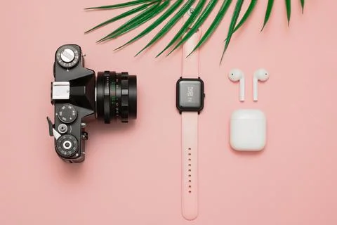 A camera, clock, bluetooth headphones and a palm leaf lie on a pink background  Stock Photos