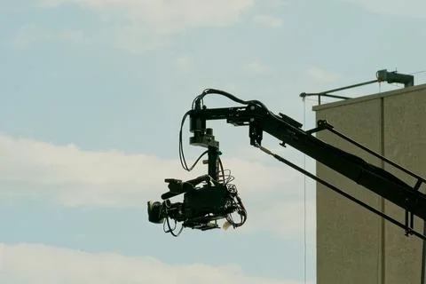 Camera crane is set up above a building to capture video footage during a shoot Stock Photos