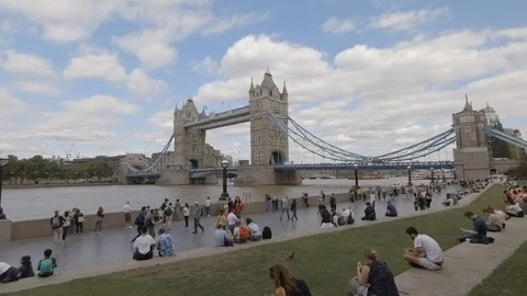 Camera cranes down from Tower Bridge to crowds sitting on grass 動画素材 93787687
