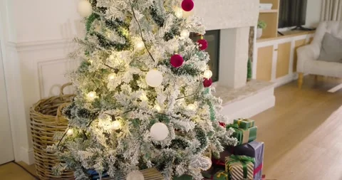 Camera is dollying and tilting up, revealing flocked Christmas tree, gifts by Stock Footage 344461104