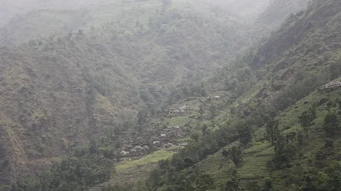 Camera drifts down from village on Himalayan mountainside to rocky river. Stock Footage 86758116