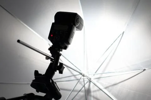 Camera flash flashes in a white umbrella in the photography studio. Stock Photos