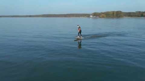 Camera flies around a man riding on a hydrofoil surfboard on large blue lake Видео 166545801