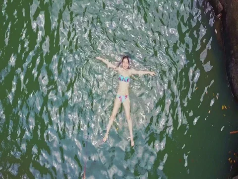 Camera Flies up over Girl Swimming in Lake under Waterfall Stock Footage