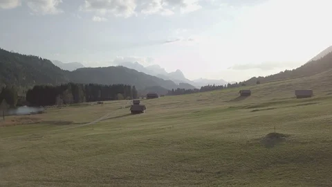 Camera flight above the green field with the wooden houses sunset time Stock Footage 89764725