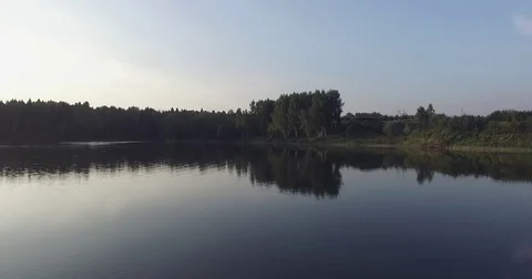 Camera flight over the lake, clear like a mirror. It reflects the trees on the Stock Footage 79407491