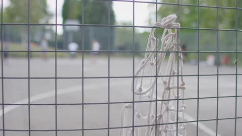 Camera focuses on an old net tied to a metal fence as players play a game of bas Stock Footage 136584616