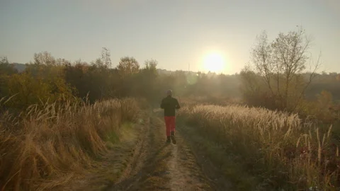 Camera is following one bold young man running on dirt road holding a map in Video stock 166155557