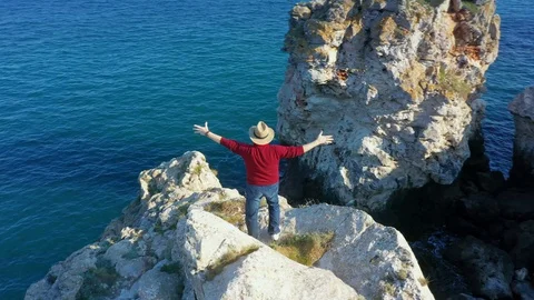Camera follows around eldery man on top of rock in the sea.  Vídeo Stock 129599591