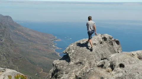 Camera follows boy running up on top of mountain summit, jumps on top of rocks Stock Footage 150398773