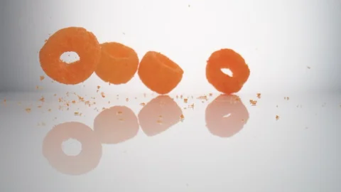 Camera follows cheese puffs falling on surface. Slow Motion.  Stock Footage 128768970