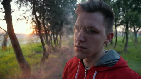 Camera follows the hand with cigarette of handsome young man smoking in the park Stock Footage 106731702