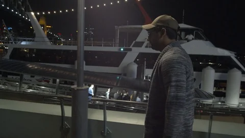 Camera Follows Man Walking along Wharf near Sydney Harbour Bridge at Night Stock Footage 107901724